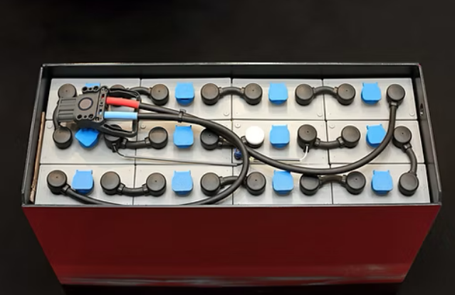 a industrial battery bank that has black bars that connect each cell together, each cell is light grey and has a blue valve in the middle.