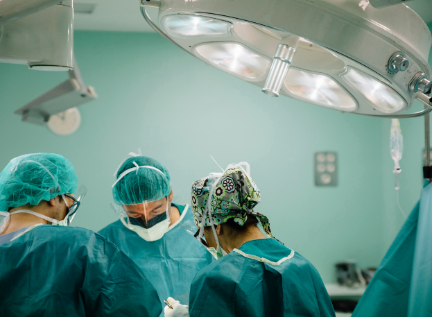 A stock image of 3 surgeons under a light wearing surgery gear. The one on the right is holding a scalpel. The surgeons take up the bottom third of the image.