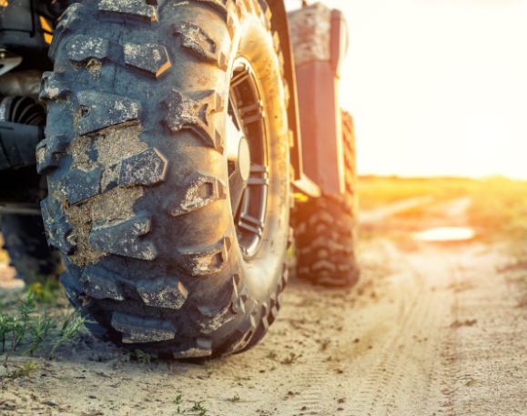 This is a stock image of an excavator, it is framed as a close up of the back wheel on the right of the vehicle, it's on a dirt road.