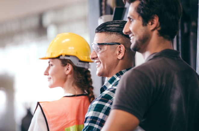 A stock image of three people, two of them are wearing safety equipment (the person furthest to the left of the image is wearing a yellow safety helmet, and the person in the middle is wearing safety goggles.) They are smiling and looking at something that is off frame.