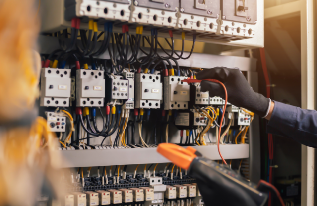 A stock image of a electrician testing the voltage of a circuit breaker that has many buttons using a orange multi-meter