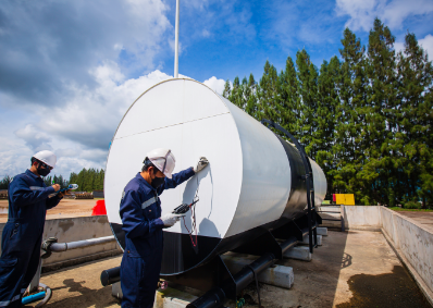 This is a stock image of two workers doing a safety test on a large diesel tank to check if it's safe for use.