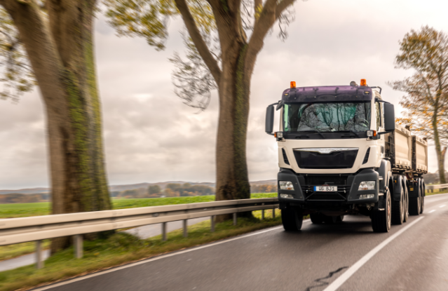 This is a stock image of a white lorry on a motorway, there are trees in the background and a field is in the distant background.